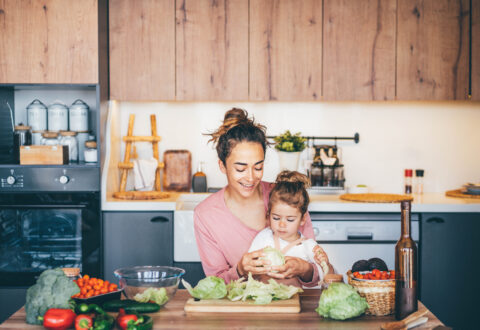 Woman having fun with her daughter while preparing salad in the kitchen.